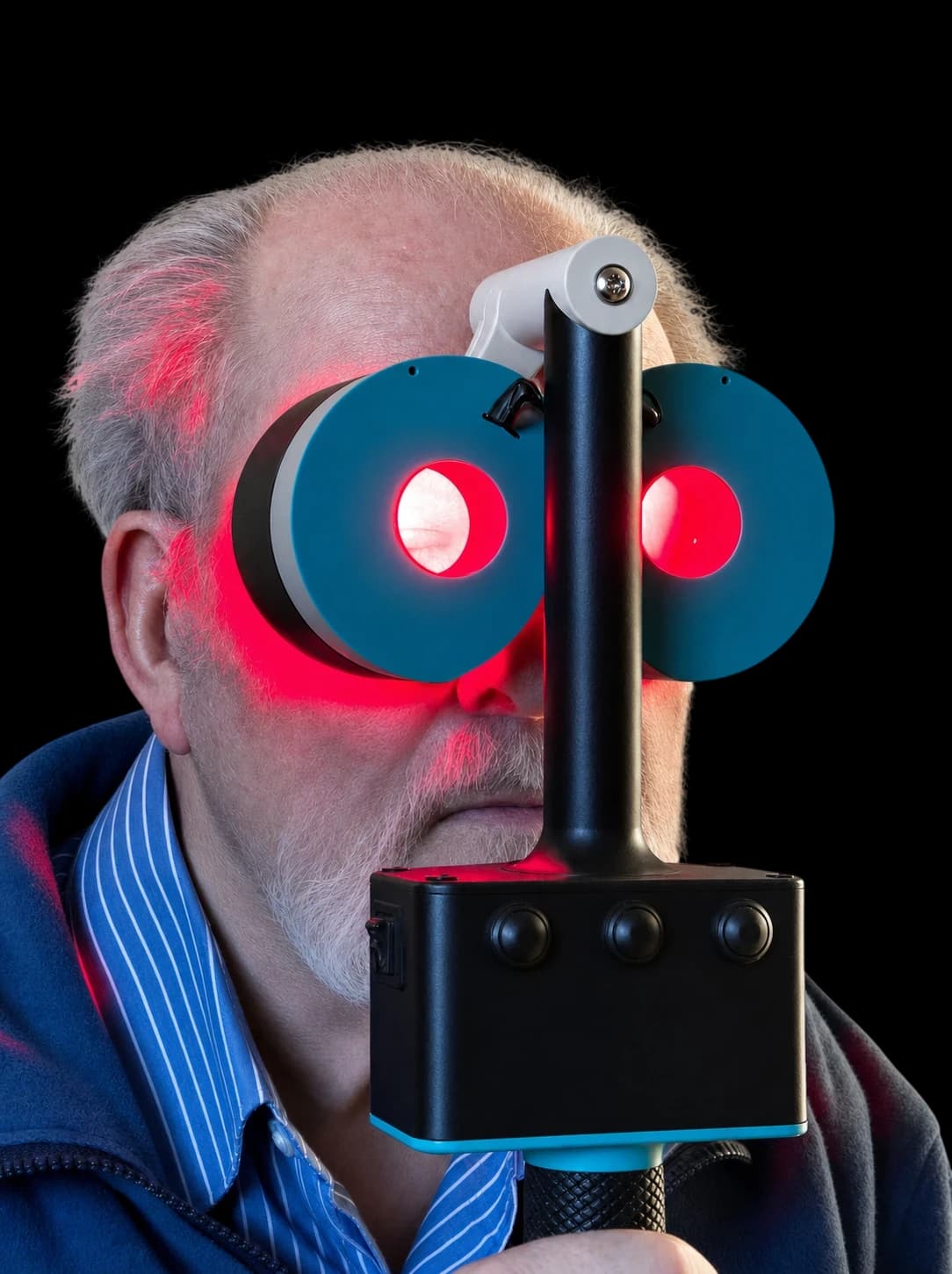 A patient using a handheld photobiomodulation device, with red therapy light visible around the eyes